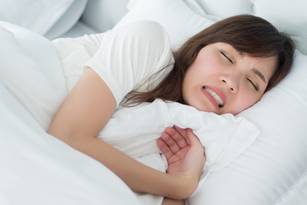 stressed woman with grinding teeth, bruxism symptoms; portrait of stressful, exhausted, tired sleeping woman grinding her teeth with stress; oral, dental care medical concept; asian adult woman model